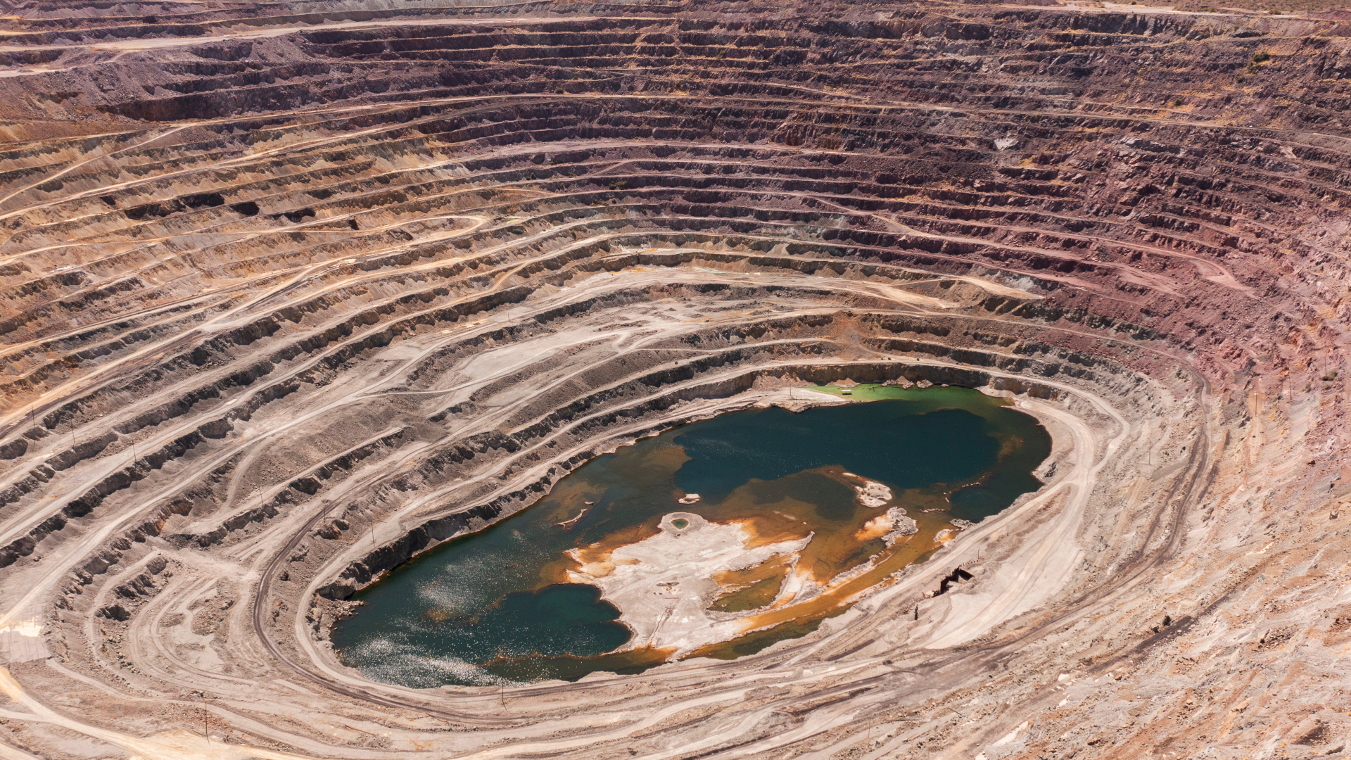 Aerial view of a large open-pit mine showcasing layered earth Aerial View of Open-Pit Mine with Layered Terrain and Water Body