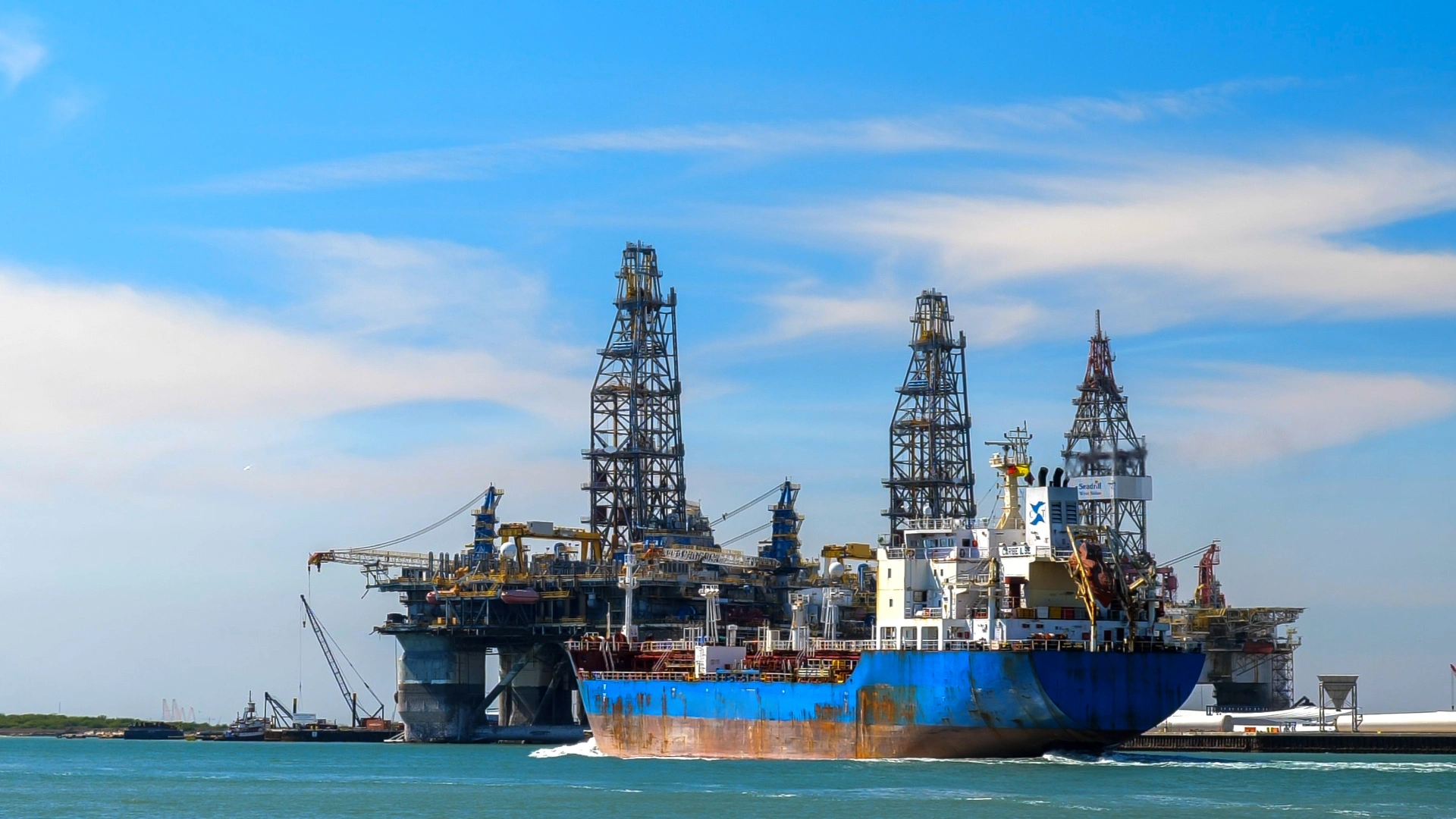 Cargo Ship Passing by Offshore Oil Drilling Rigs Blue cargo ship near offshore rigs