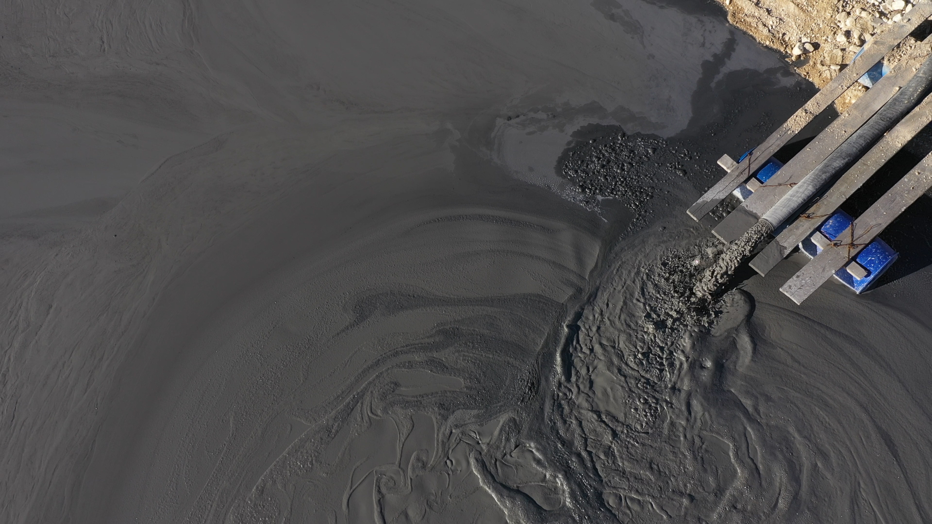 Aerial View of Slurry Discharge into Dark Muddy Area Aerial view of slurry being discharged from a pipe