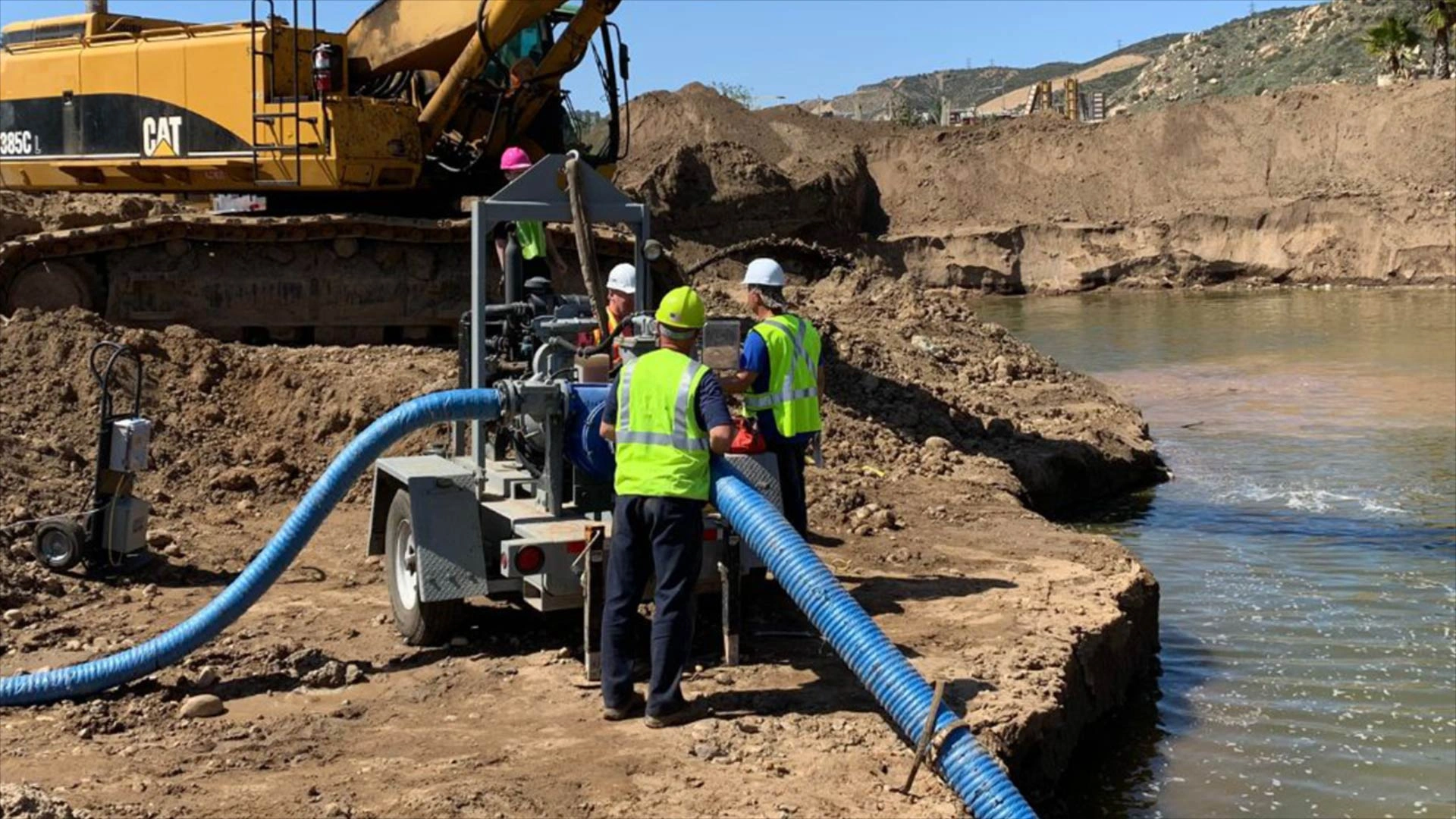 Construction team operating slurry pump near river Construction workers operating a large slurry pump system near a riverbank