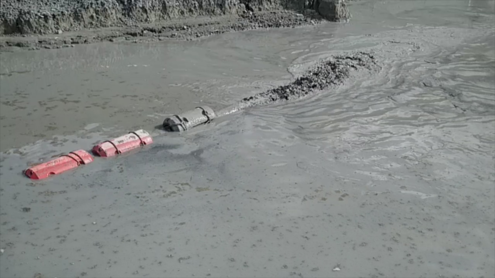 Slurry Discharge Pipe in Muddy Water with Floating Barriers A pipe releasing thick slurry into a muddy water surface,