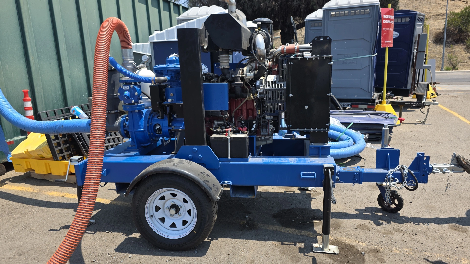 Blue Machinery Trailer with Pump and Hoses in Construction Area A blue machinery trailer equipped with a pump, hoses, and a battery