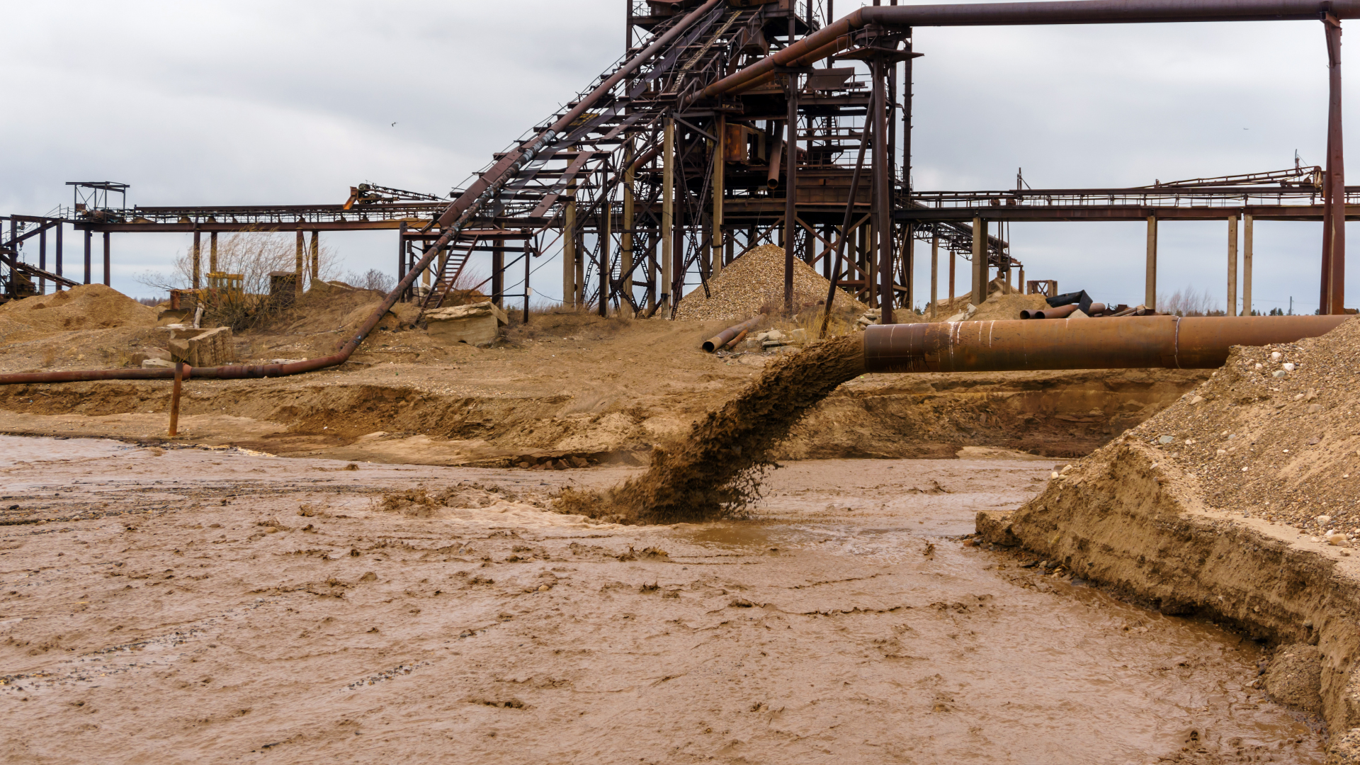 Industrial Pipe Discharging Muddy Water into Flowing Stream Muddy discharge with industrial backdrop