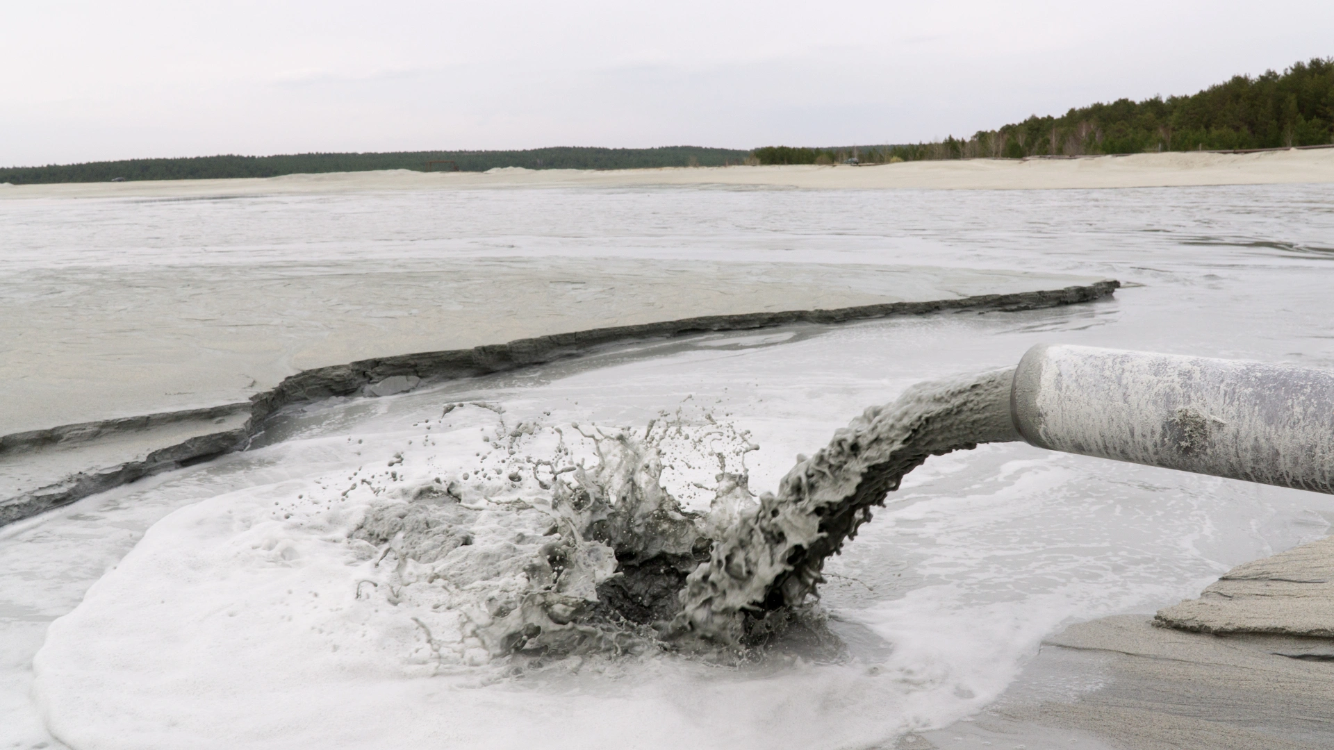 Discharge of Gray Slurry from Pipe into Shallow Water A pipe discharging a thick, gray slurry into a shallow body